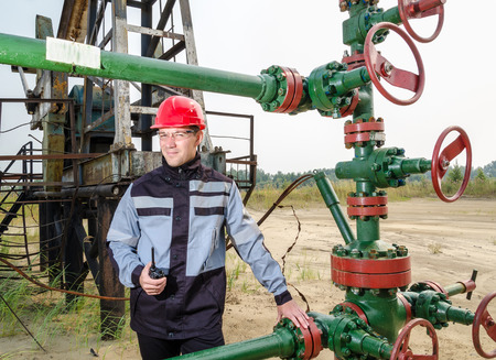 Oilfield worker near wellhead wearing red helmet and work clothes holding the radio. Oil and gas concept.の写真素材