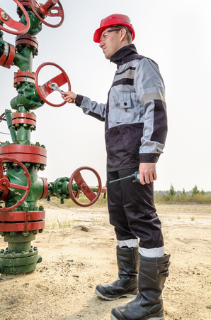 Oilfield worker repairing wellhead valve with the wrench, wearing red helmet and work clothes. Oil and gas concept.の写真素材