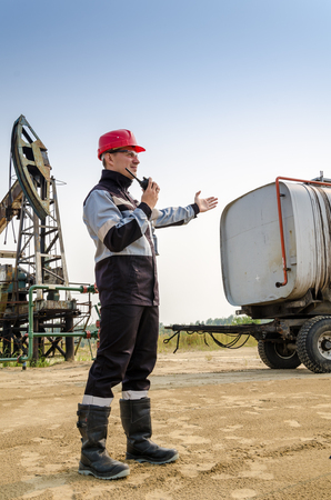 Worker talking on the radio near pump jack and tank trailer in the oilfield. Oil and gas concept.の写真素材