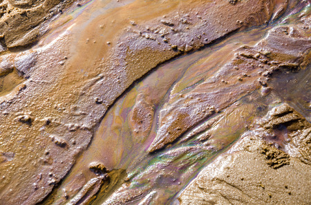 Rainbow oil slick on the sand. Textured background. Pollution of water and ground concept.の写真素材