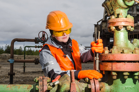 Woman engineer in the oilfield repairing wellhead with the wrench wearing orange helmet and work clothes. Oil and gas concept.の写真素材