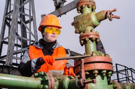 Woman engineer in the oilfield repairing wellhead with the wrench wearing orange helmet and work clothes. Oil and gas concept.の写真素材