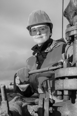 Woman engineer in the oil field repairing wellhead with the wrench wearing orange helmet and work clothes. Oil and gas concept. Black and white.の写真素材