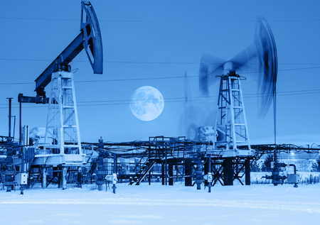 Working oil pump jack at night time. Full moon. Oilfield during winter. Oil and gas concept. Toned.の写真素材