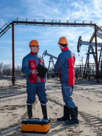 Two workers in the oilfield. Pump jack, pipeline and wellhead background. Oil and gas concept.の写真素材