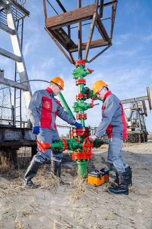 Workers in the oilfield repairing wellhead with the wrench. Pump jack and wellhead background. Oil and gas concept.の写真素材