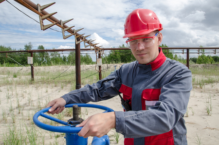 Worker near wellhead valve holding radio and wearing red helmet in the oilfield. Pipeline background.  Oil and gas concept.の写真素材