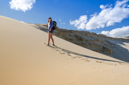 Young beautiful woman backpacker traveling in the desert. Sandy dunes and blue sky on sunny summer day. Travel, adventure, freedom concept.の写真素材