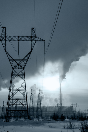 Gas power station in cold winter landscape during sunset. Pipes with smoke. Power transmission tower foreground. Energy industry concept. Toned. の写真素材