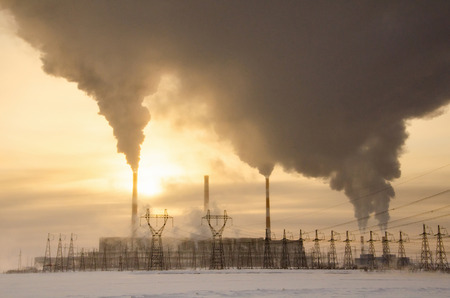 Gas power plant in cold winter landscape during sunset. Pipes with smoke. Power transmission tower foreground. Energy industry concept. Toned.の写真素材