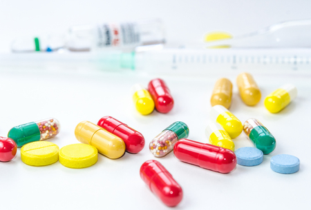 Colorful medicine pills, drugs and capsules with syringe and ampule on a white background. Selective focus. Close-up macro shot.の写真素材