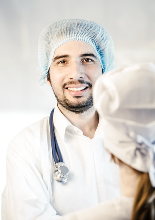 Group portrait of medical doctors in hospital, one looking at camera and smiling. Men wearing surgeon coat and woman wearing white cap. Focus on man doctor. Toned.の写真素材