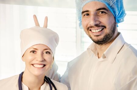 Group portrait of mixed aged medical doctors standing in hospital, looking at camera, kidding and smiling. Men wearing surgeon coat and woman wearing white cap and coat. Toned.の写真素材