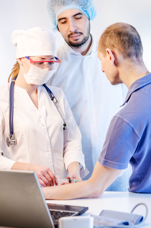Group portrait of medical doctors in hospital having consultation with patient and making injection. Man wearing surgeon coat and woman wearing white cap. Focus on woman doctor.の写真素材