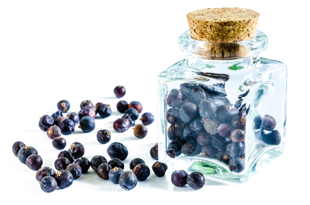 Dry juniper berries in glass bottle and heap of juniper near it isolated on white background. Closeup macro shot.の写真素材
