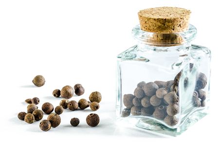 Dry allspice in glass bottle and in a heap isolated on white background. Closeup macro shot.の写真素材