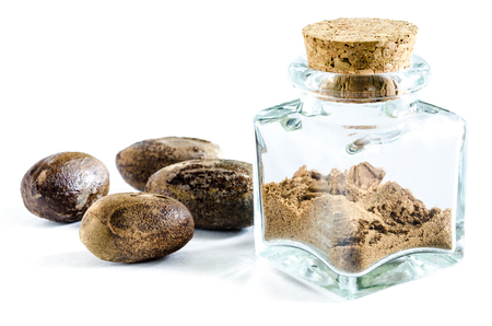 Dry nutmeg powder in glass bottle and whole nutmeg near it isolated on white background. Closeup macro shot.の写真素材
