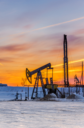 Pump jack, wellhead and oil rig during sunset in the oilfield. Winter period. Oil and gas concept.の写真素材
