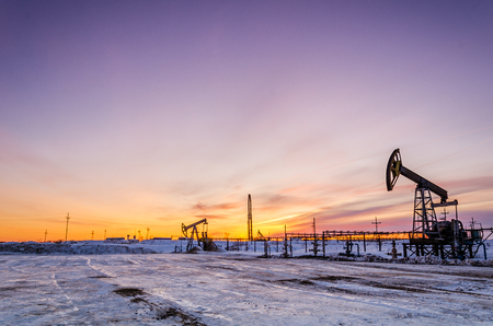 Pump jack, wellhead, pipeline and oil rig during sunset in the oilfield. Winter period. Oil and gas concept.の写真素材