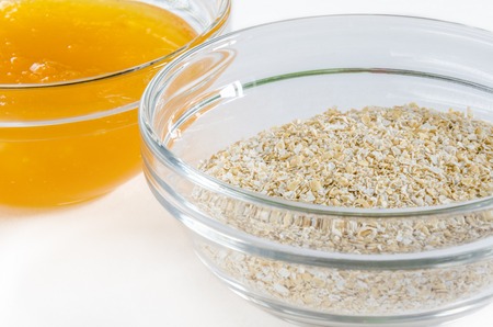 Oat bran and honey in a glass bowl isolated on white background. Closeup shot. Healthy food concept.の写真素材