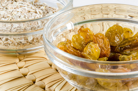Oat flakes and raisins in a glass bowl on straw hot pad. Closeup shot. Healthy food concept.の写真素材