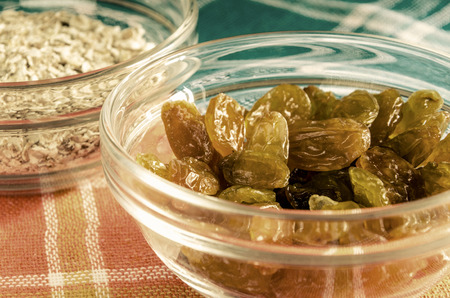 Oat flakes and raisins in a glass bowl on colorful dishcloth. Closeup shot. Healthy food concept. Toned.の写真素材