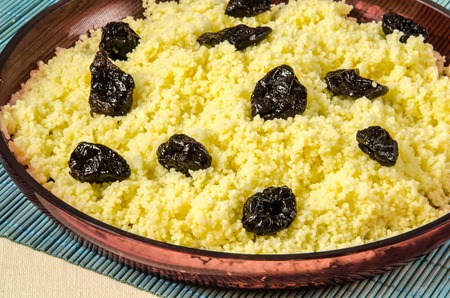 Plate with freshly cooked Moroccan couscous with prunes on blue straw backgroundの写真素材