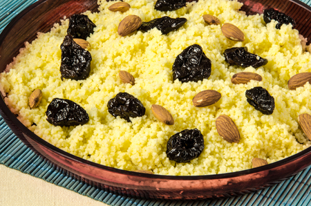 Plate with freshly cooked Moroccan couscous with almond and prunes on blue straw backgroundの写真素材