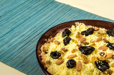 Plate with freshly cooked Moroccan couscous with almond and prunes on blue straw backgroundの写真素材