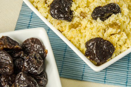 Plate with freshly cooked Moroccan couscous and with prunes on blue straw backgroundの写真素材