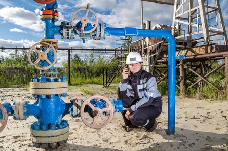 Woman engineer in the oilfield talking on the radio wearing white helmet and work clothes....