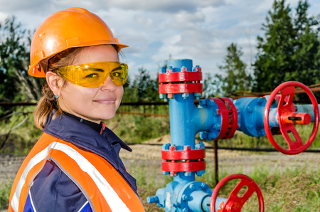 Woman worker in the oilfield near wellhead, wearing orange helmet and work clothes. Industrial site background. Oil and gas concept.の写真素材