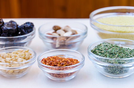 Variety of ingredients for couscous cooking such as prune, hot pepper, cedar nut, herbs in glass bowlsの写真素材