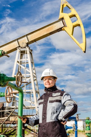 Woman engineer in the oilfield near pump jack wearing white helmet and work clothes. Industrial site background. Oil and gas concept.の写真素材