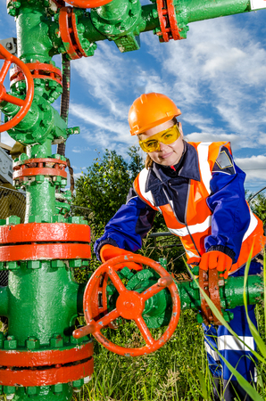 Woman worker in the oilfield repairing wellhead wearing orange helmet and work clothes. Industrial site background. Oil and gas concept.の写真素材