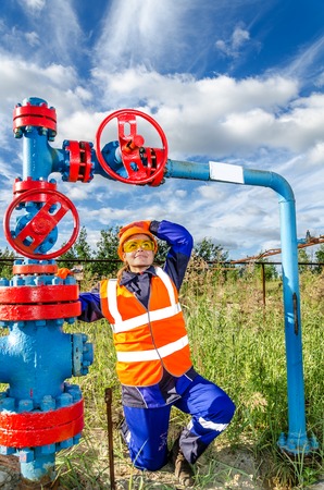 Woman worker in the oilfield near wellhead, wearing orange helmet and work clothes. Industrial site background. Oil and gas concept.の写真素材
