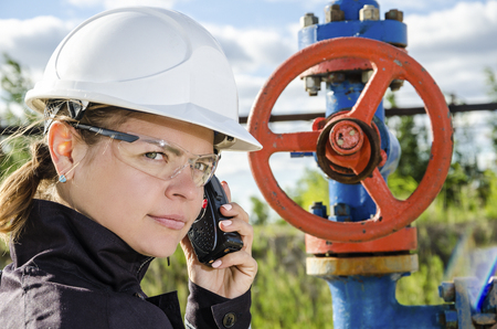 Woman engineer in the oilfield talking on the radio wearing white helmet and work clothes. Toned.の写真素材