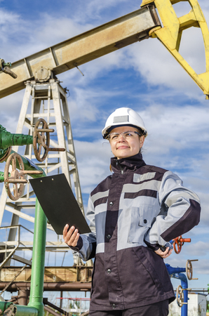 Woman engineer in the oilfield talking on the radio wearing white helmet and work clothes. Toned.の写真素材