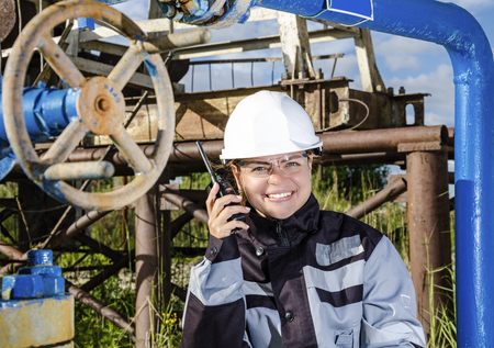 Woman engineer in the oilfield talking on the radio wearing white helmet and work clothes. Toned.の写真素材