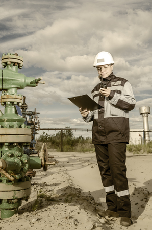 Woman engineer in the oilfield talking on the radio wearing white helmet and work clothes. Toned.の写真素材