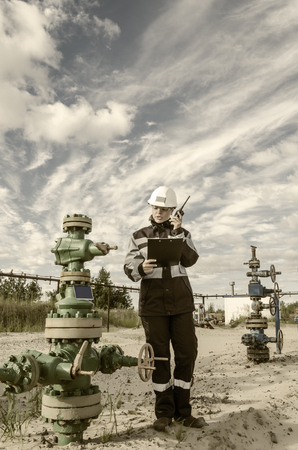 Woman engineer in the oilfield talking on the radio wearing white helmet and work clothes. Toned.の写真素材