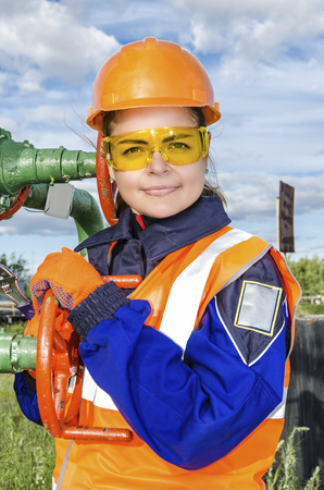 Woman worker in the oilfield repairing wellhead wearing orange helmet and work clothes.の写真素材