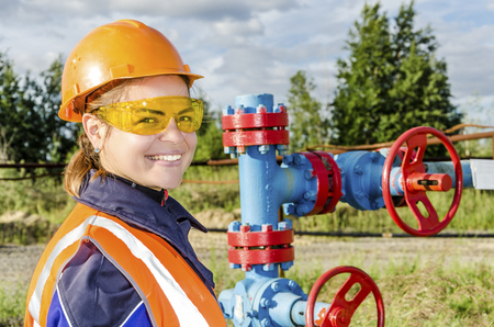 Woman worker in the oilfield repairing wellhead wearing orange helmet and work clothes.の写真素材