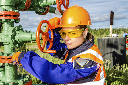 Woman worker in the oilfield repairing wellhead wearing orange helmet and work clothes.の写真素材