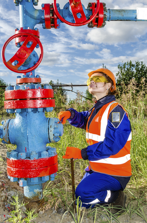Woman worker in the oilfield repairing wellhead wearing orange helmet and work clothes.の写真素材