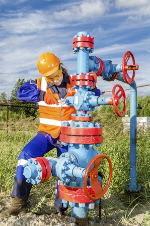 Woman worker in the oilfield repairing wellhead wearing orange helmet and work clothes.の写真素材