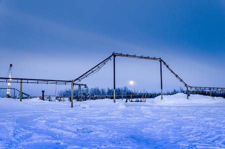 Pump jack, wellhead, pipeline and oil rig during moon eclipse in the oilfield. Winter period. Oil and gas concept. Toned.の写真素材
