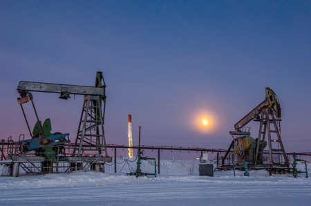 Pump jack, wellhead, pipeline and oil rig during moon eclipse in the oilfield. Winter period. Oil and gas concept. Toned.の写真素材