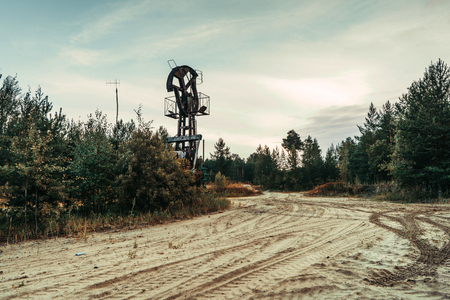 Old rusty pump jack in the oilfield situated in the beautiful forest. Environmental pollution. Oil and gas concept.の写真素材