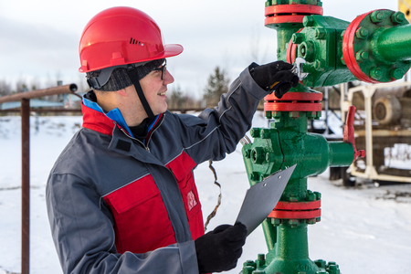 Man worker in the oilfield near pump jack and wellhead, wearing helmet and work clothes. Industrial site background. Oil and gas concept.の写真素材